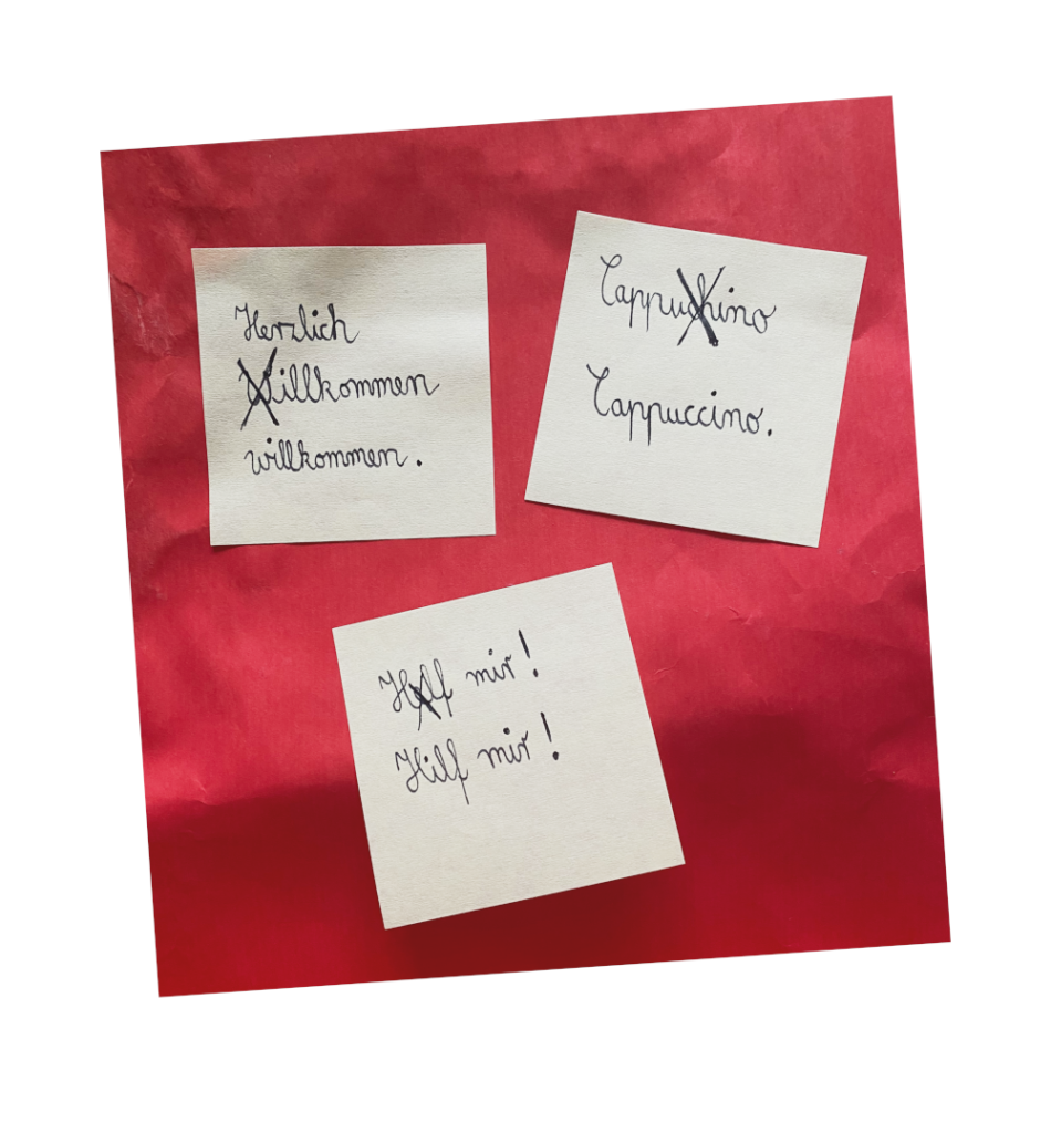 Post-It-Aufkleber, die falsche Schreibweisen der Ausdrücke "Herzlich willkommen", Cappuccino und "hilf mir" zeigen.