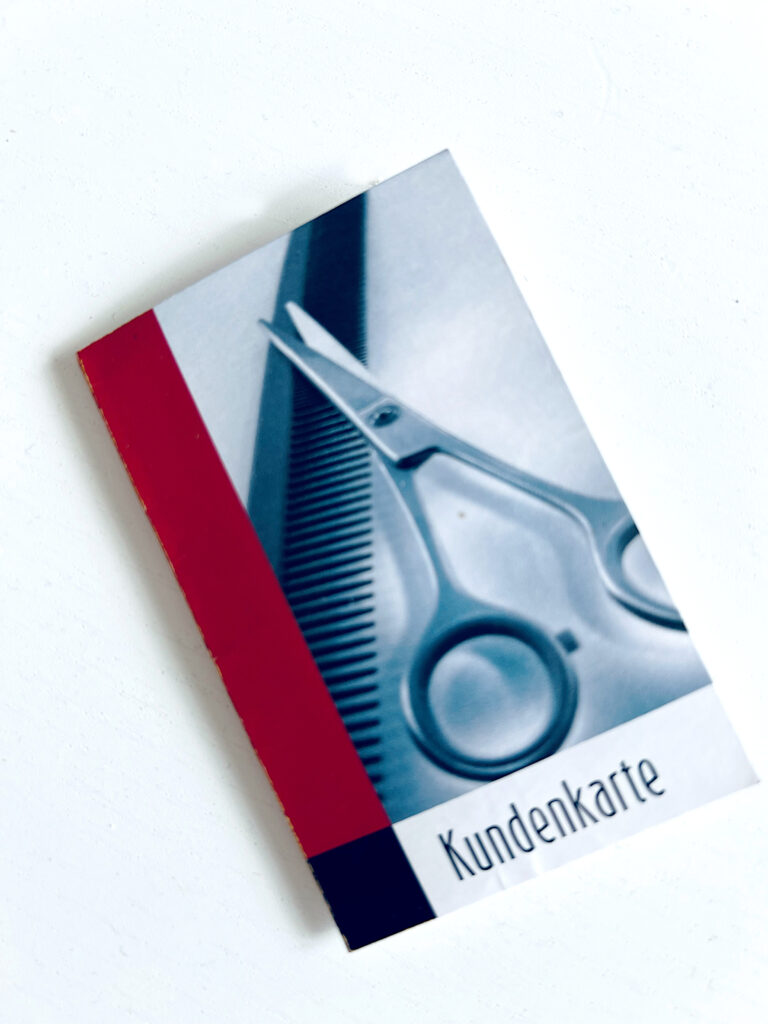 Das Foto zeigt eine kleine Kundenkarte zum Aufklappen, die vorne einen Kamm und eine Schere ziert.