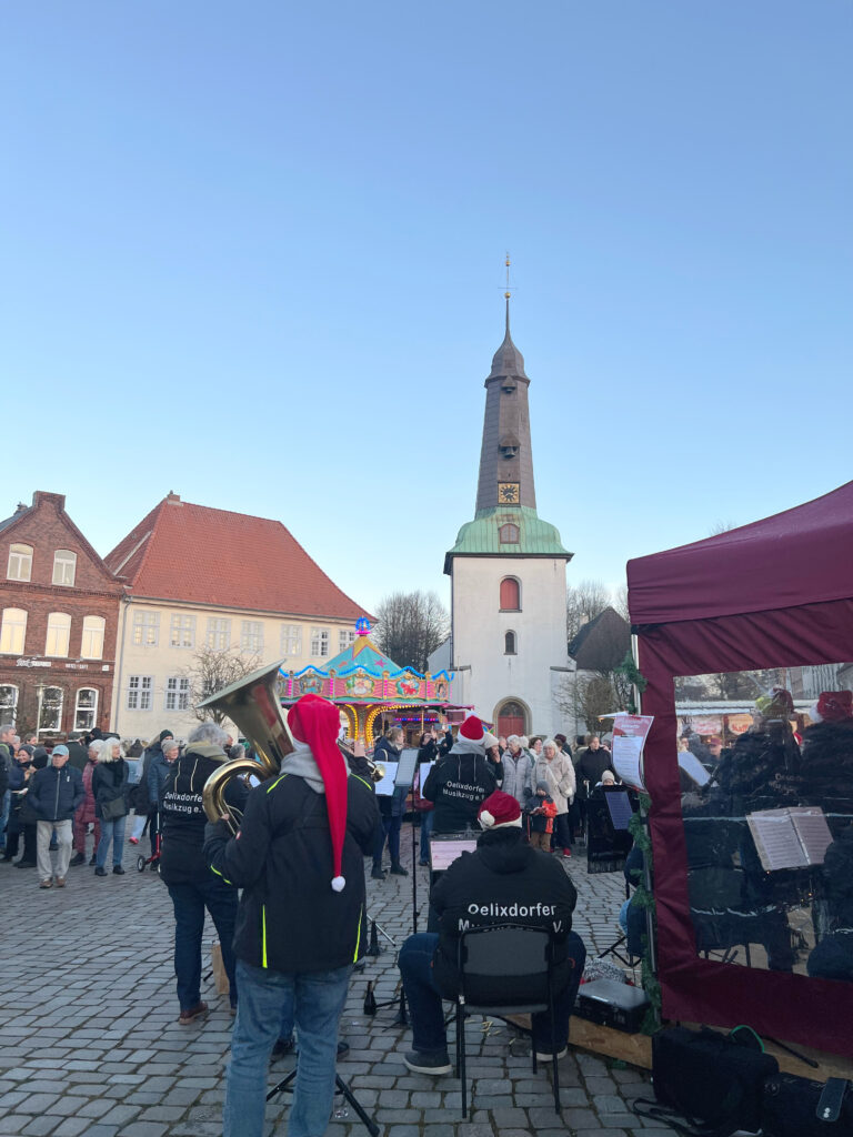 Blick mitten vom Marktplatz in Glückstadt an der Elbe aus auf die Kirche, im Vordergrund ist der Oelixdorfer Musikzug zu sehen, der Weihnachtslieder spielt.