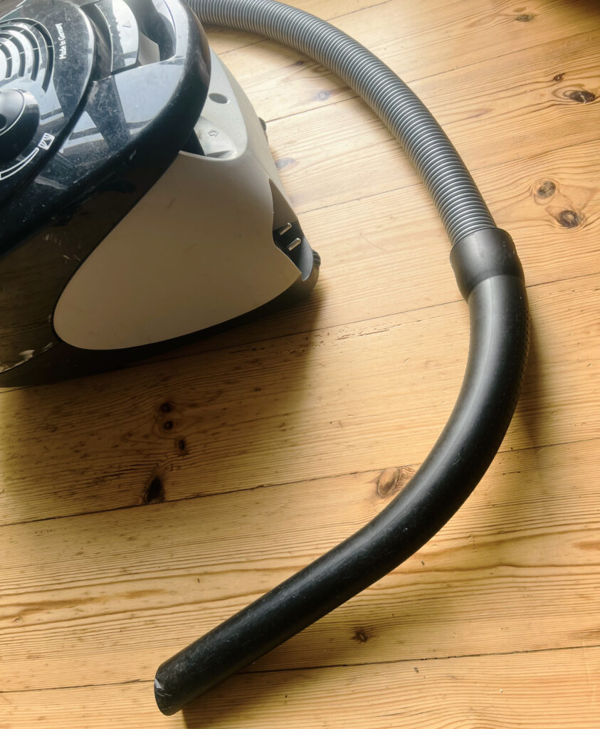 Der hintere Teil eines handelsüblichen Staubsaugers, schon etwas in die Jahre gekommen, mit Kratzern und Spuren. Aber auch der Rüssel ist zu sehen und leistet immer noch beste Dienste.