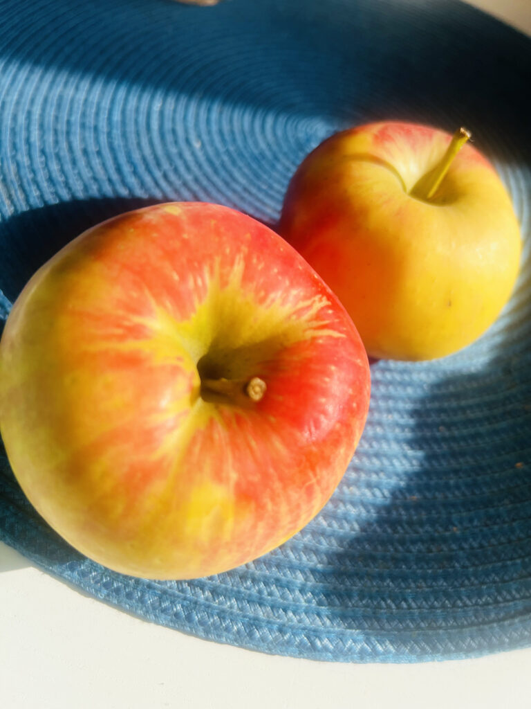 Zwei schöne Äpfel leuchten in der Sonne auf einem Tisch mit einem dunkelblauen Set drapiert.