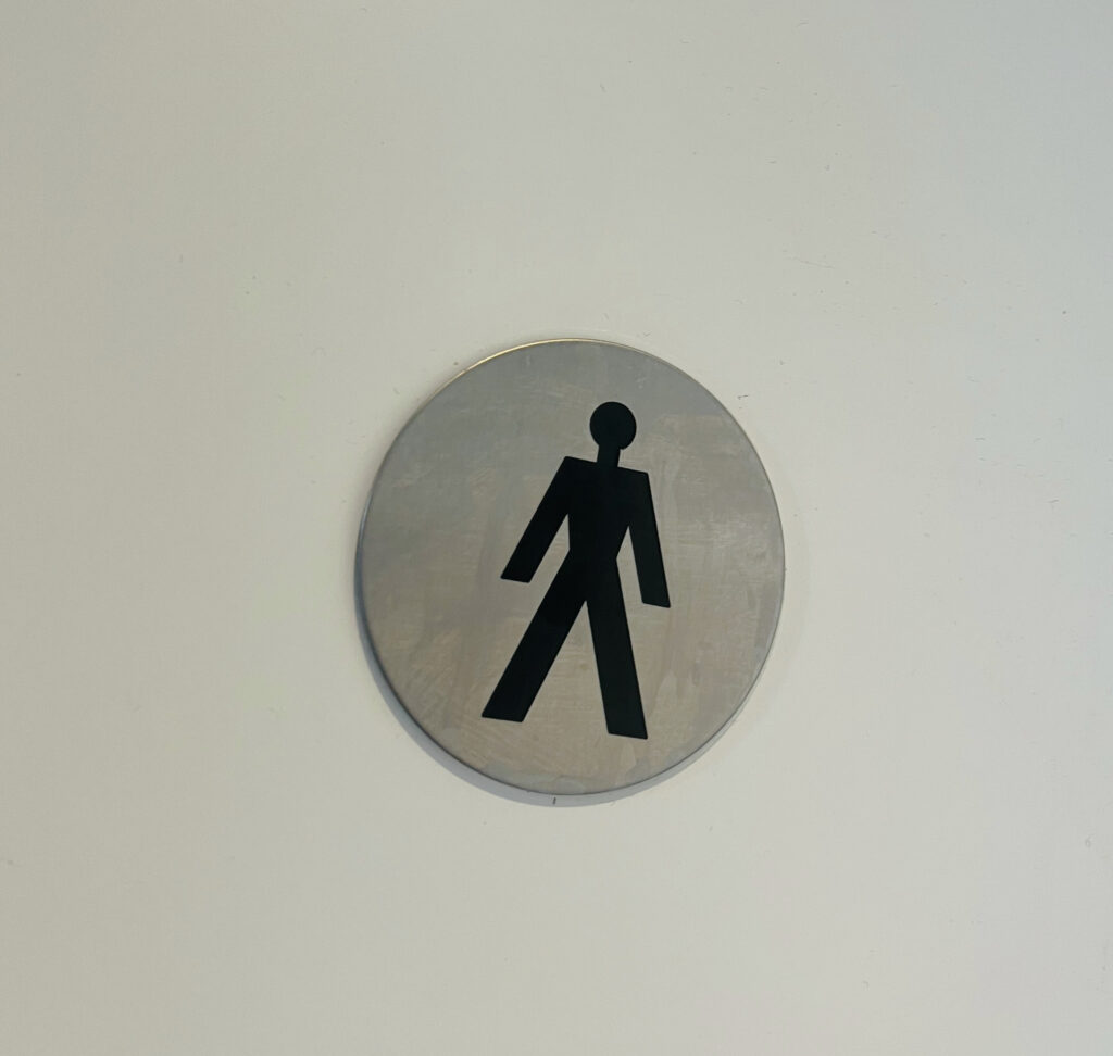 Das Zeichen, das an der Tür einer öffentlichen Toilette prangert, ein schwarzes Männchen auf einem Metalluntergrund.